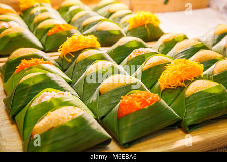 Thai dessert: dolci di riso appiccicoso con uova al vapore con crema pasticcera con topping varietà avvolto con foglie di banano package visualizzati sul ripiano in street fo Foto Stock