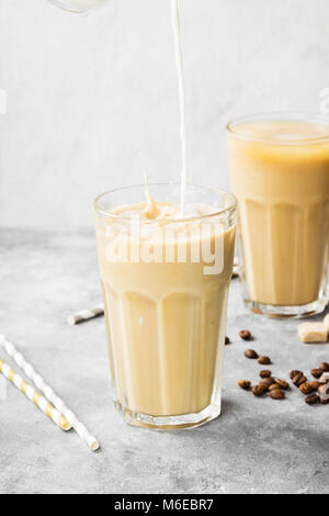 Versare il latte nel caffè ghiacciato in un bicchiere alto su sfondo grigio Foto Stock