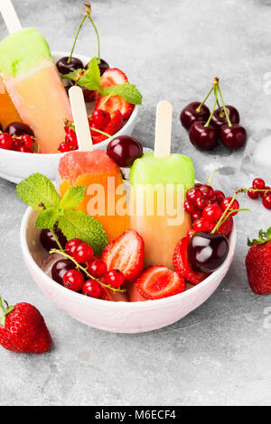 Multi-popsicles colorati con Fragola, ribes rosso e ciliegia su uno sfondo grigio Foto Stock