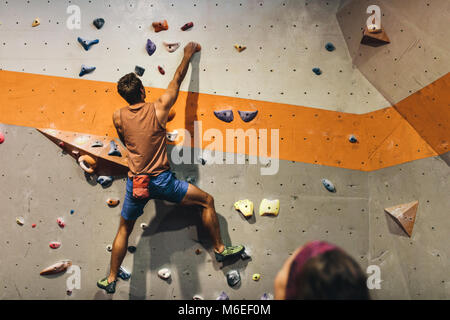 L'uomo bouldering in una palestra di roccia al coperto centro mentre una donna guarda a. Scalatore praticare arrampicate su roccia in una piscina palestra di arrampicata. Foto Stock