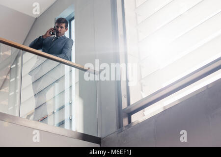 Imprenditore appoggiata sulla ringhiera in edificio per uffici e parlare sullo smartphone. Bassa angolazione persona d'affari facendo una telefonata. Foto Stock