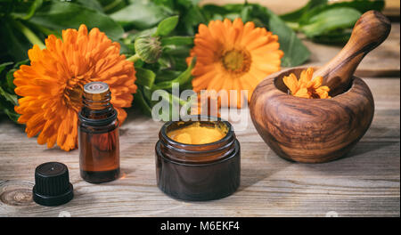 Calendula prodotti. Olio essenziale, unguento e un mortaio su una tavola di legno, fresche blooming calendula sfondo, Foto Stock