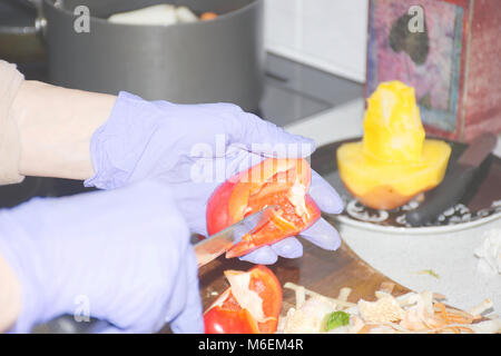 Donna mani guanti nella preparazione del cibo in cucina.Il taglio di peperoni rossi ,rimuovendo i semi dal peperone rosso.tagliare la frutta di mango e pentole in background. Foto Stock