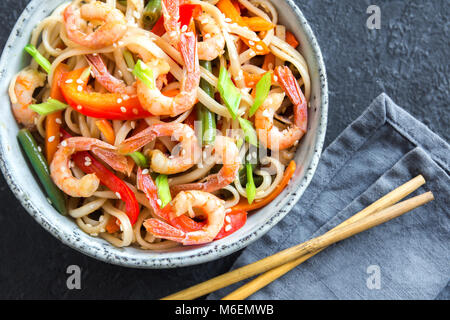 Stir fry con udon noodles, gamberi (gamberetti) e verdure. Asian cibo sano, pasto, friggere in un recipiente su sfondo nero, copia dello spazio. Foto Stock