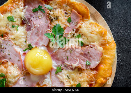 Pizza Carbonara sulla pietra nera dello sfondo. Pizza italiana Carbonara con pancetta, uova e formaggio vicino. Foto Stock