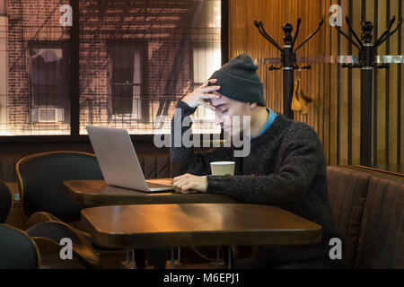 Stanco esaurito man mano tiene su forhead presso il cafe. Giovane maschio persona con gli occhi chiusi in cafe nella parte anteriore del computer portatile Foto Stock