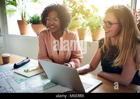 Due diversi giovani designer sorridere mentre seduti insieme durante una riunione del consiglio di amministrazione in un ufficio moderno Foto Stock