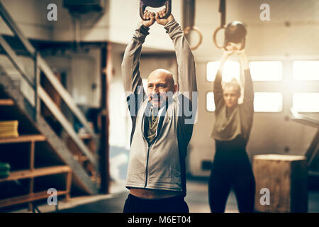 Montare uomo maturo in sportswear sorridente e oscillazione un peso durante un esercizio di classe in una palestra Foto Stock