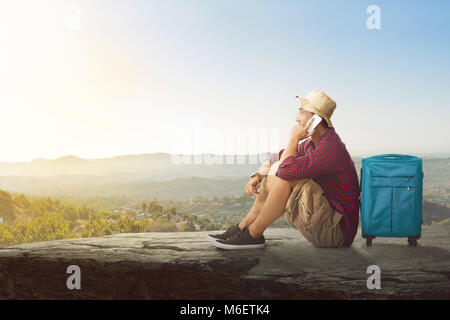 Giovani asiatici turistico con telefono cellulare rilassante sulla sommità della roccia su sfondo cielo Foto Stock