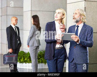 Delle società multinazionali persone in piedi nella hall del moderno edificio cercando con tavoletta digitale a portata di mano. Foto Stock