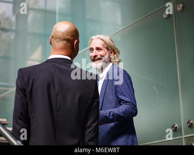 Caucaso e latino corporate executives avente una conversazione mentre salite le scale in ufficio moderno edificio. Foto Stock