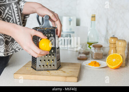 Reticolo di scorza di cedro. Mani femminili utilizzare grattugia per rendere la buccia di limone in ambiente cucina Foto Stock