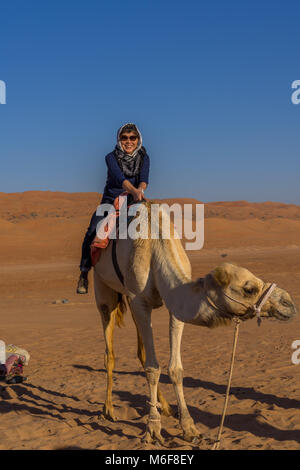 Donna torist a dorso di un cammello nel deserto Oman con felice e faccia sorridente sul suo. Foto Stock