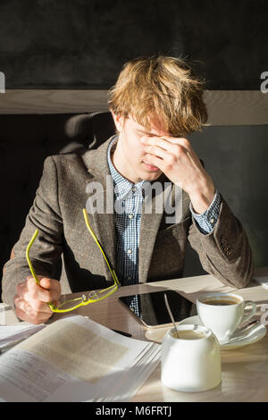 Stanco studente maschio si toglie gli occhiali lettura e sfrega gli occhi durante la pausa caffè presso il ristorante. Bel giovane uomo intelligente si appoggia di fare wor Foto Stock