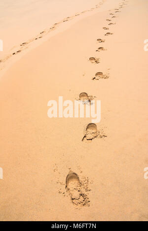Piedi stampe nella sabbia di una spiaggia che conduce a una distanza o un orizzonte che simboleggia un movimento e un senso di direzione a Plettenberg Bay nel sud Afr Foto Stock