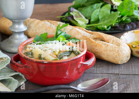 Abbondante fagioli bianchi e zuppa di verdure stufato di carne servita in un tegame di coccio rosso con una focaccia di grano pane francese. Scena alimentare, in casa di bontà. Foto Stock