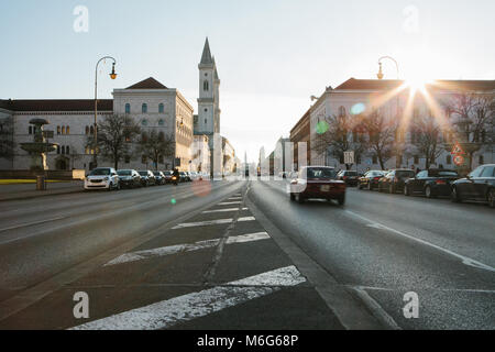 Vista della strada sulla strada Leopoldstrasse a Monaco di Baviera - la capitale del Land Baviera nella Repubblica federale di Germania. Fast sfocata auto moto su sfondo al tramonto. Foto Stock