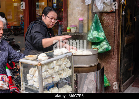 Una donna cuochi bao bun, un pane cotto a vapore street food snack sul sentiero di Hanoi, Vietnam Foto Stock