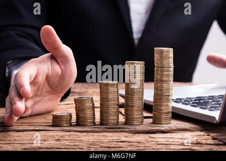 Close-up di un impilati monete d oro e commercianti la mano sulla scrivania in legno Foto Stock