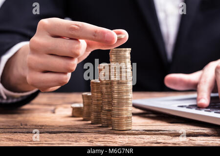 Close-up di commercianti la mano collocando un gettone sulla crescente di pile di monete Foto Stock