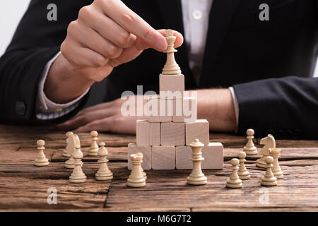Close-up di un imprenditore la mano ponendo re pezzo degli scacchi sulla parte superiore dei blocchi di legno Foto Stock