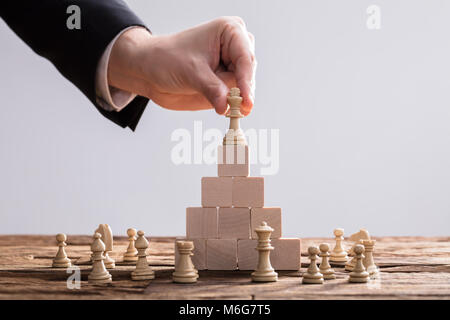 Close-up di un imprenditore la mano ponendo re pezzo degli scacchi sulla parte superiore dei blocchi di legno Foto Stock