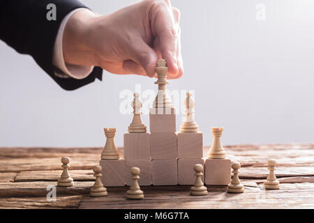 Close-up di un imprenditore la mano ponendo re pezzo degli scacchi sulla parte superiore dei blocchi di legno Foto Stock