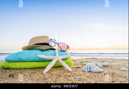 Estate accessori come occhiali da sole, asciugamani, cappello, solare, conchiglie e stella di mare sulla spiaggia di sabbia in Portogallo Foto Stock