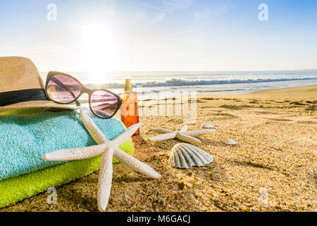 Estate accessori come occhiali da sole, asciugamani, cappello, solare, conchiglie e stella di mare sulla spiaggia di sabbia in Portogallo Foto Stock