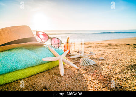 Estate accessori come occhiali da sole, asciugamani, cappello, solare, conchiglie e stella di mare sulla spiaggia di sabbia in Portogallo Foto Stock