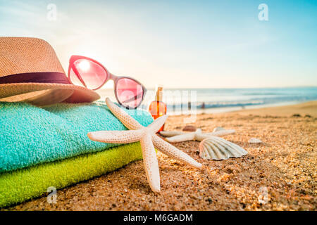 Estate accessori come occhiali da sole, asciugamani, cappello, solare, conchiglie e stella di mare sulla spiaggia di sabbia in Portogallo Foto Stock