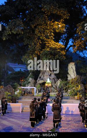 Giovani felici e solenne Hmong ragazze vestiti in abiti tradizionali tenendo candele e fiori celebrare la Vergine Maria a Sapa chiesa di pietra di notte. Foto Stock