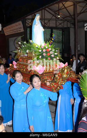 Il vietnamita donne vestite di lunghi abiti blu che trasportano la statua della Vergine Maria su un altare di legno circondato da fiori di notte alla chiesa di pietra Sapa. Foto Stock