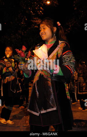 Giovani felici e solenne Hmong ragazze vestiti in abiti tradizionali tenendo candele e fiori celebrare la Vergine Maria a Sapa chiesa di pietra di notte. Foto Stock