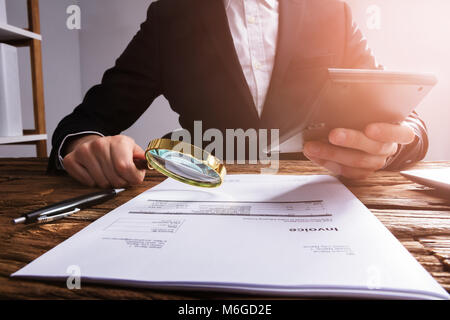 Commercianti la mano analizzando Bill con lente di ingrandimento sulla scrivania in legno Foto Stock