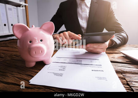 I mediatori controllo fattura con Rosa Piggybank sulla scrivania in legno Foto Stock