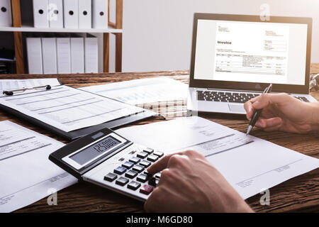 Close-up di un imprenditore la mano il calcolo di Bill con il laptop sulla scrivania in legno Foto Stock