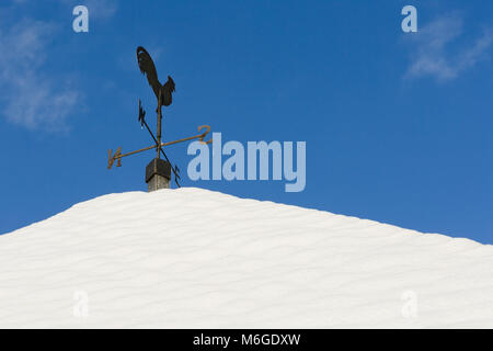 Galletto banderuola rivolta verso est sulla coperta di neve di piastrelle con cielo blu. Foto Stock