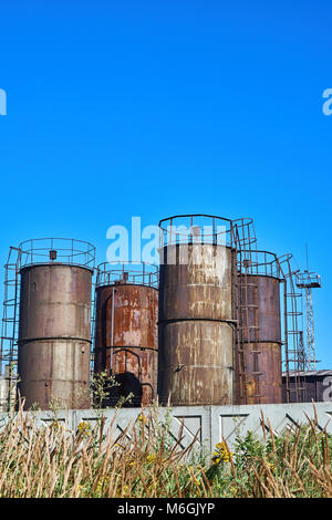 Vecchi serbatoi di stoccaggio di carburante industriali arrugginiti contro il cielo blu Foto Stock