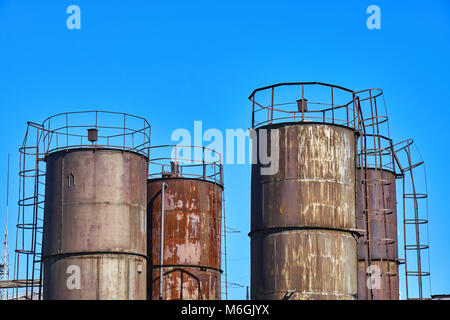 Vecchi serbatoi di stoccaggio di carburante industriali arrugginiti contro il cielo blu Foto Stock