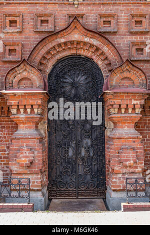 Pareti in mattoni riccamente dettagliate incornicia una maestosa porta in metallo con intricati lavori in ferro battuto della vecchia cappella Foto Stock