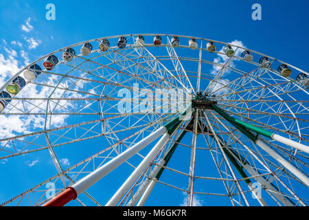 Enorme ruota panoramica contro il cielo nuvoloso nel parco divertimenti con vista dall'angolo basso Foto Stock