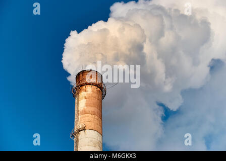 Tubo di fabbrica alto e grungo che emette spesso fumo bianco contro il cielo blu senza nuvole Foto Stock