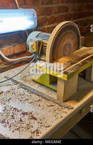 Levigatrice a disco da banco con lampada nella polvere dopo il lavoro in officina Foto Stock