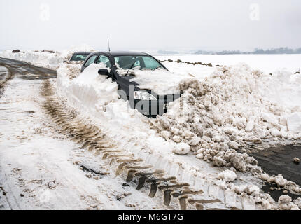 East Lothian, Scozia, Regno Unito, 4 marzo 2018. Regno Unito Meteo: due vetture sepolto nella neve sul Drem a Haddington Road dopo la nevicata come risultato delle condizioni meteorologiche estreme evento, soprannominato il "Bestia da est. Alta banchi di neve crea un passaggio stretto Foto Stock