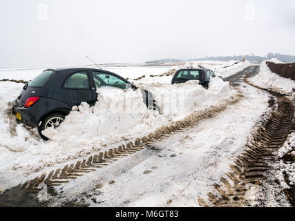 East Lothian, Scozia, Regno Unito, 4 marzo 2018. Regno Unito Meteo: due vetture sepolto nella neve sul Drem a Haddington Road dopo la nevicata come risultato delle condizioni meteorologiche estreme evento, soprannominato il "Bestia da est. Alta banchi di neve crea un passaggio stretto Foto Stock