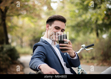 Giovane imprenditore attraente di scattare una foto con il suo smartphone all'aperto in un parco. Felice, sorridente Foto Stock