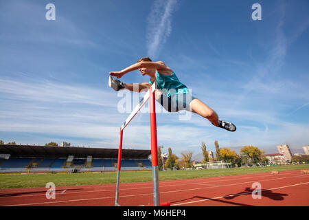 Basso angolo di vista determinato atleta maschio saltando su una ostacoli Foto Stock