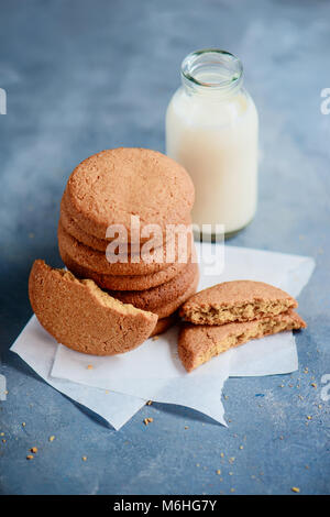 I cookie con segni di morsi e una bottiglia di latte su una luce blu tavolo da cucina con copia spazio. Sana colazione minimalista. Foto Stock