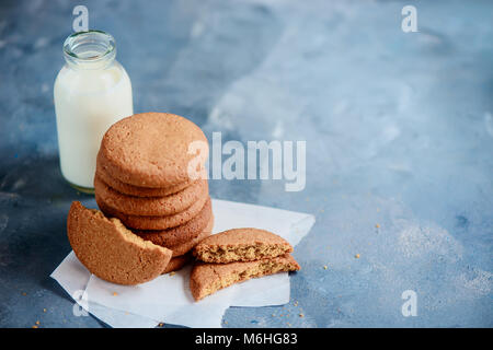 Testata con i fiocchi d'avena i biscotti con segni di morsi e una bottiglia di latte su una luce blu tavolo da cucina con copia spazio. Foto Stock